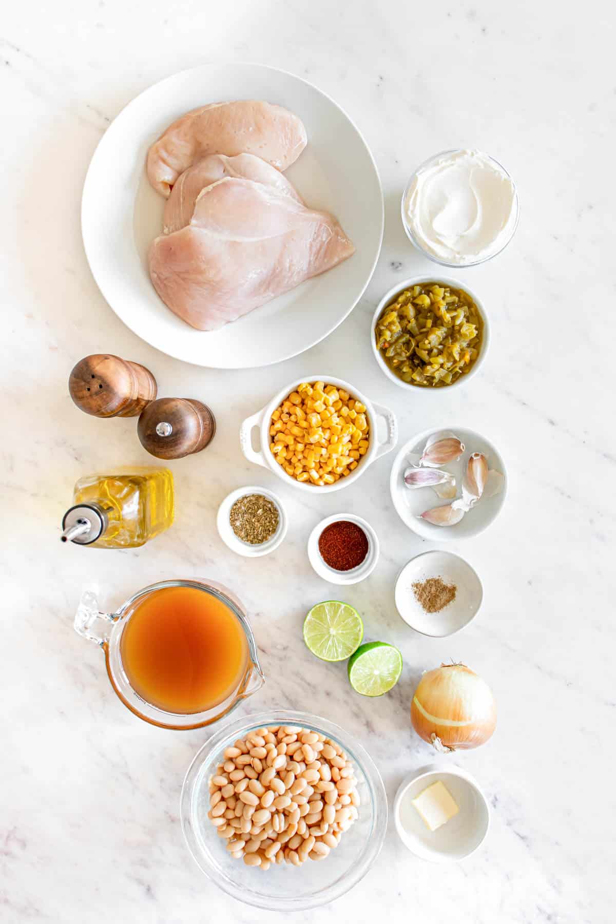 Ingredients for white chicken chili laid out on a kitchen counter, including chicken breasts, spices, corn, beans, and other condiments.