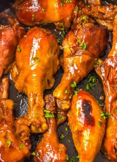 A pan of glazed and baked Dr. Pepper chicken drumsticks garnished with fresh herbs.