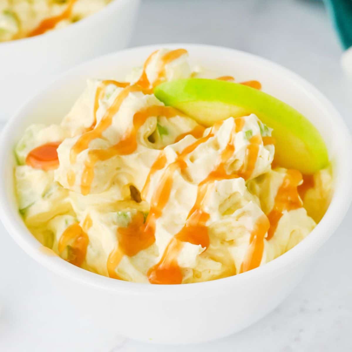 A bowl of creamy caramel apple salad with pieces of apple and a caramel drizzle on top.