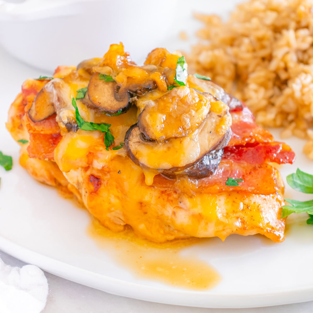 A plate with a serving of Alice Springs Chicken (Outback Copycat) topped with melted cheese, mushrooms, and herbs, accompanied by a side of brown rice.
