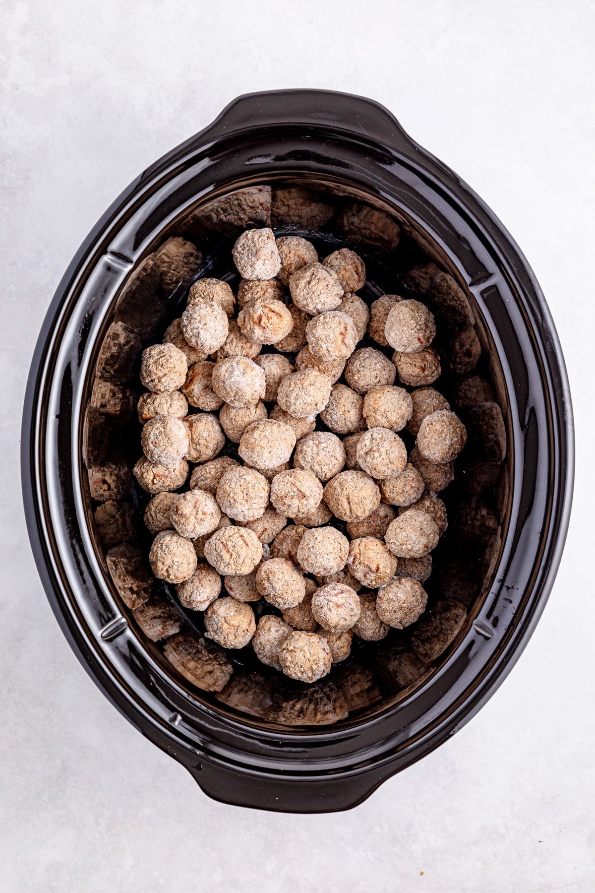 A black slow cooker filled with raw, round, seasoned sausage balls for Salisbury Steak Meatballs recipe