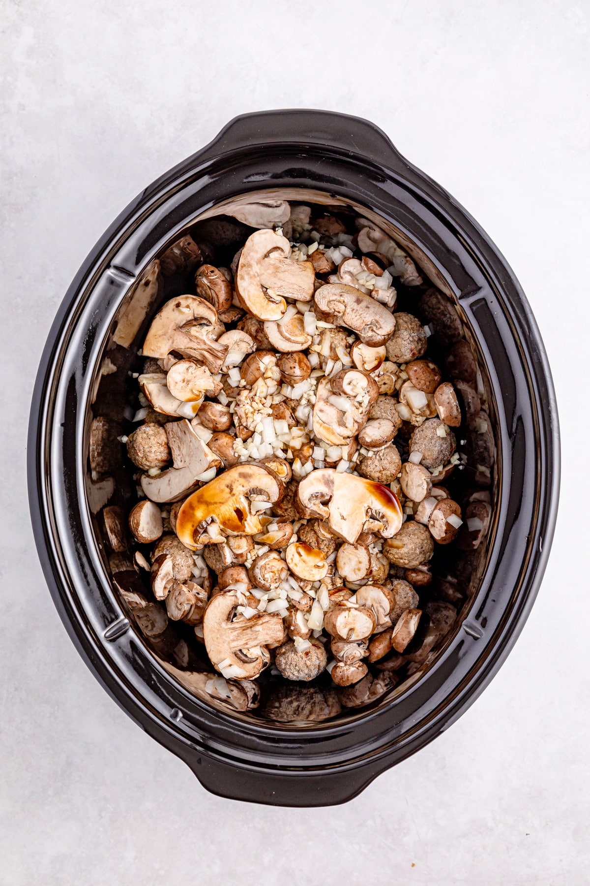 A slow cooker filled with sliced mushrooms and chopped onions on a light surface for Salisbury Steak Meatballs recipe