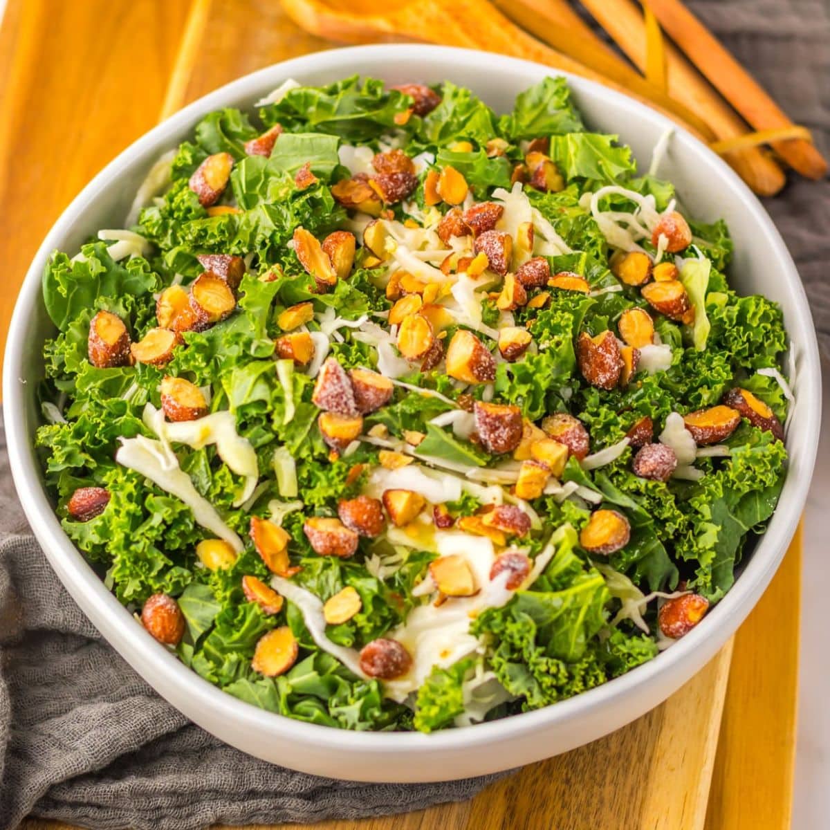 A salad featuring kale, shredded cheese, and chopped nuts in a white bowl.