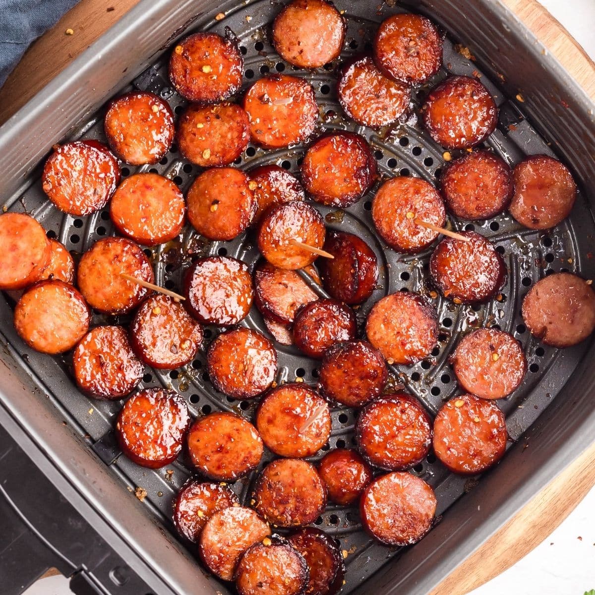 Sliced air fryer kielbasa pieces, some with toothpicks, are arranged in a single layer inside an air fryer basket.
