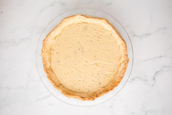 Adding a creamy filling on a white plate and marble surface to make a coconut pie.