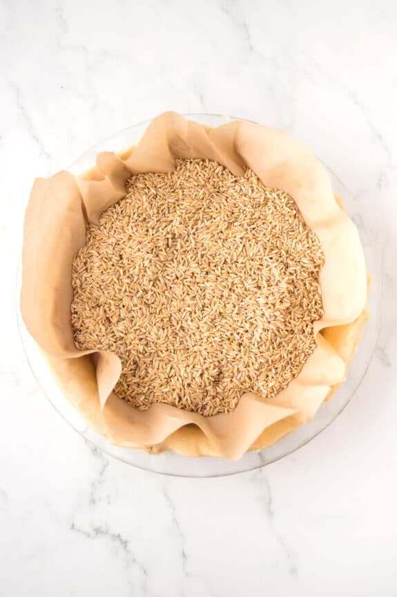 A pie dish lined with parchment paper and filled with uncooked rice, used as pie weights on an unbaked pie crust for Coconut pie recipe