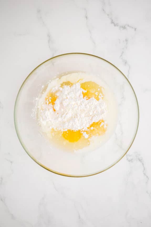 First step in making a filling for the coconut pie recipe is to use a glass bowl and combine eggs, milk, and a mound of white flour on a white marble surface.