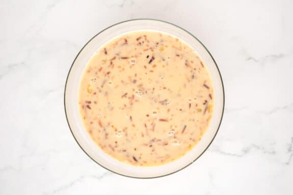 A glass bowl filled with 1 cup milk, coconut milk, sugar, salt, and toasted coconut ingredients for Coconut Pie.
