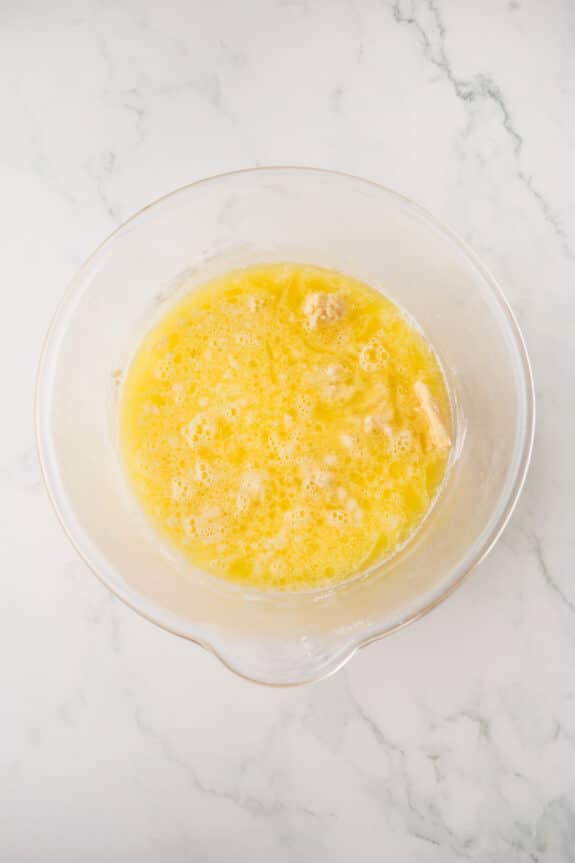 A glass mixing bowl containing a melted butter and other ingredients, on a white marble surface for White Texas Sheet Cake recipe