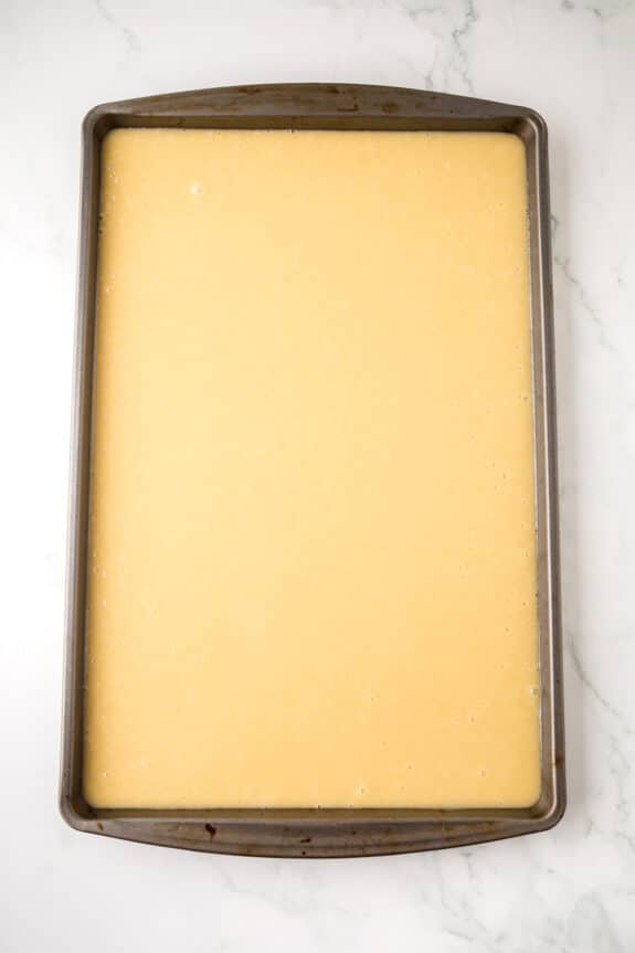 A rectangular metal baking sheet filled with a smooth, unbaked yellow batter on a white marble surface for White Texas Sheet Cake recipe