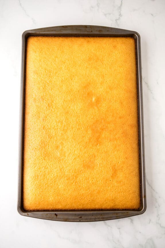 A rectangular White Texas Sheet Cake in a metal baking pan rests on a white marble surface.
