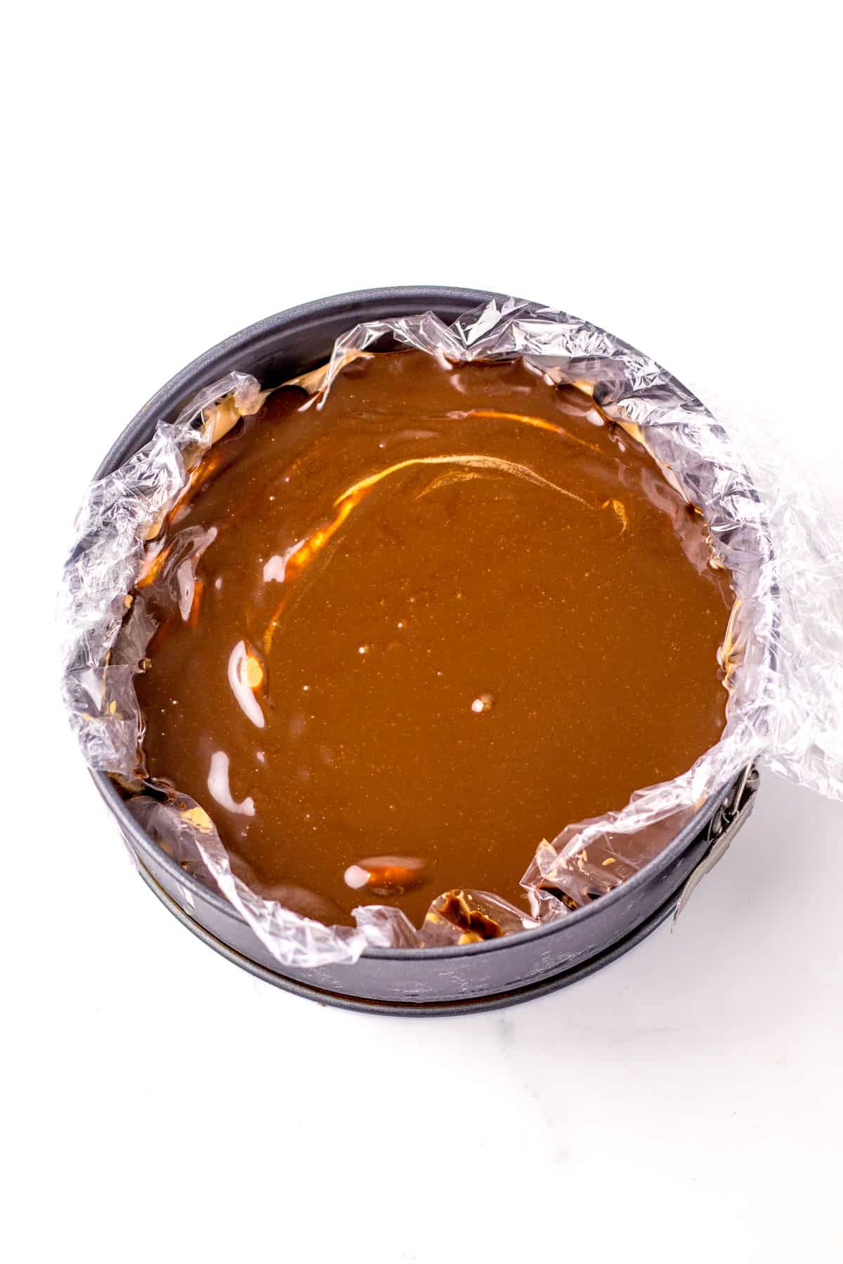A round baking pan with hot fudge lined with plastic wrap, filled with smooth for Dairy Queen Ice Cream Cake recipe.