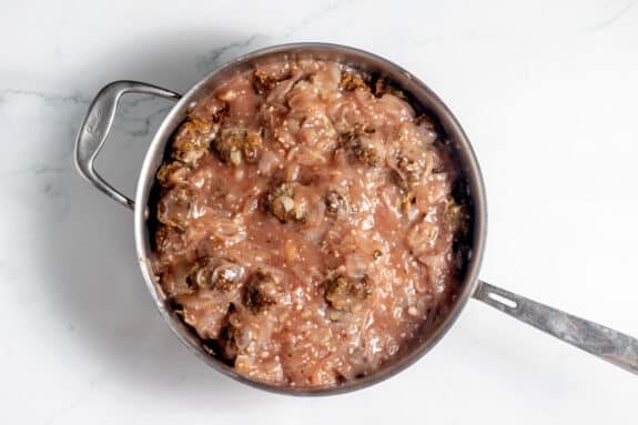 A metal saucepan filled with meatballs and shredded cabbage in a thick, reddish-brown sauce, placed on a white marble surface.
