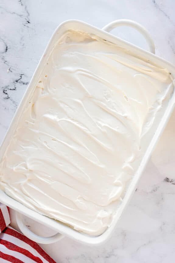 A white rectangular baking dish filled with a with smooth, swirled whipped cream, on a marble surface for Cherries in the Snow