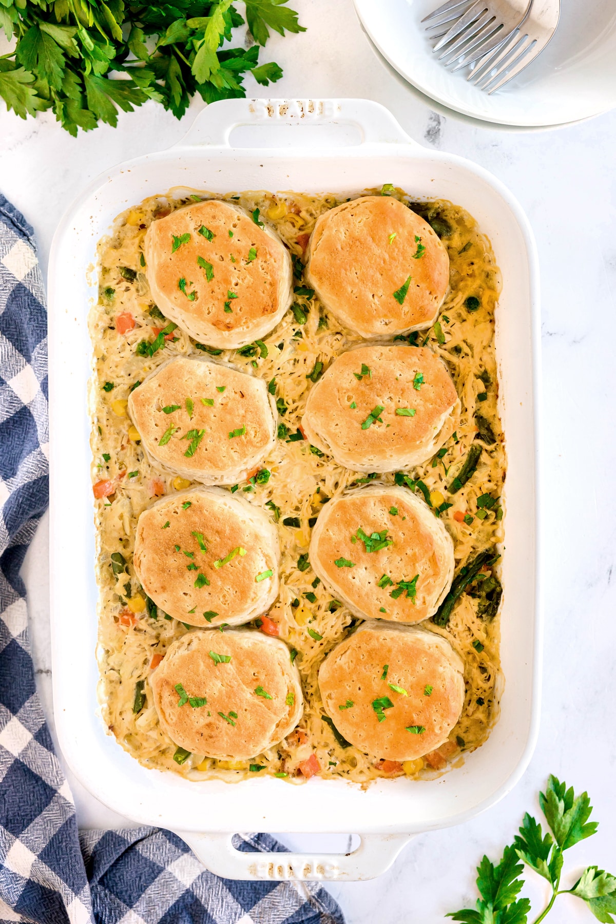 Chicken Pot Pie Casserole with creamy chicken and vegetable mixture, topped with nine golden biscuits, garnished with chopped herbs. A fork, plate, and napkin are nearby.