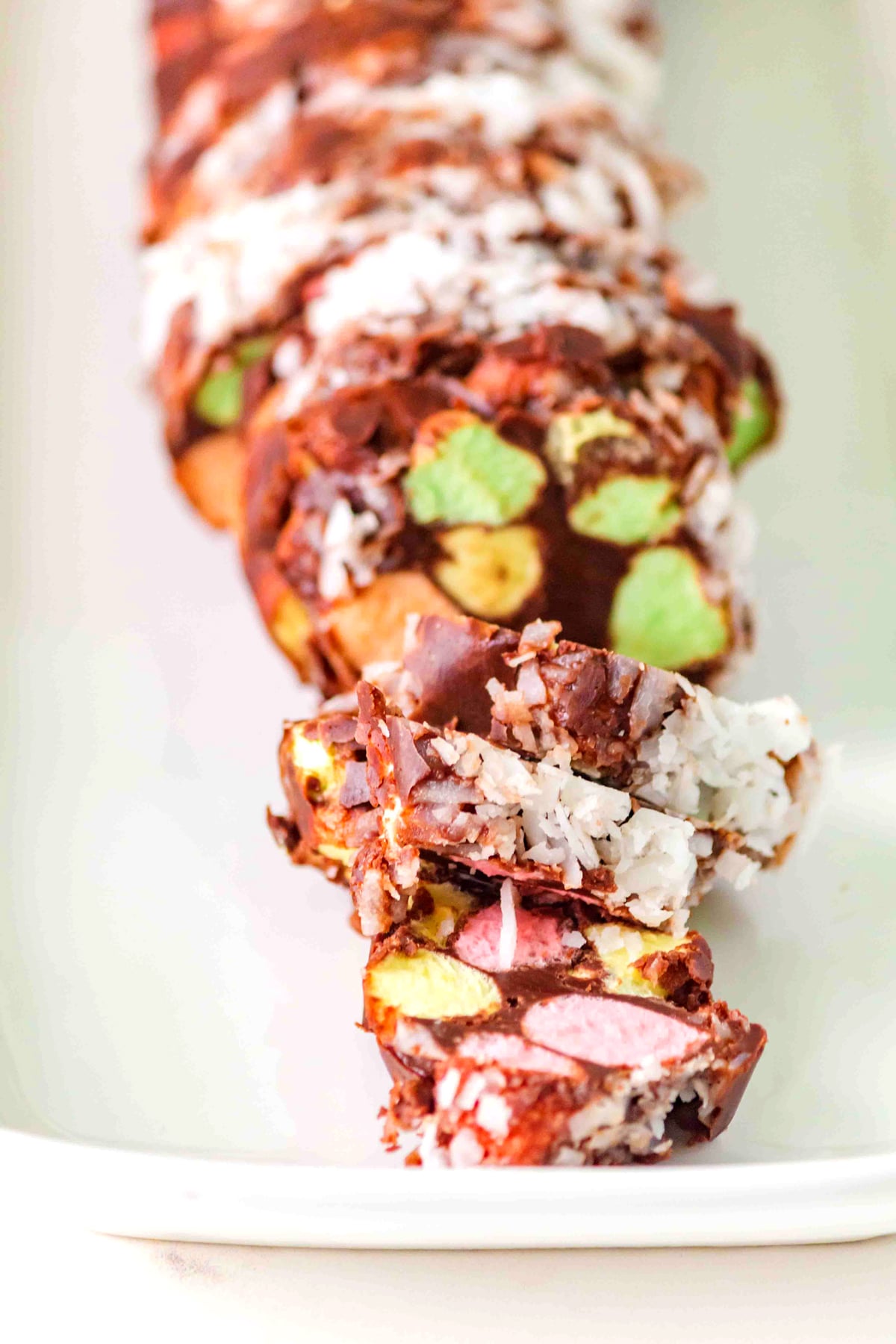 Sliced Church Window Cookies log with colorful marshmallows and coconut on a white plate.