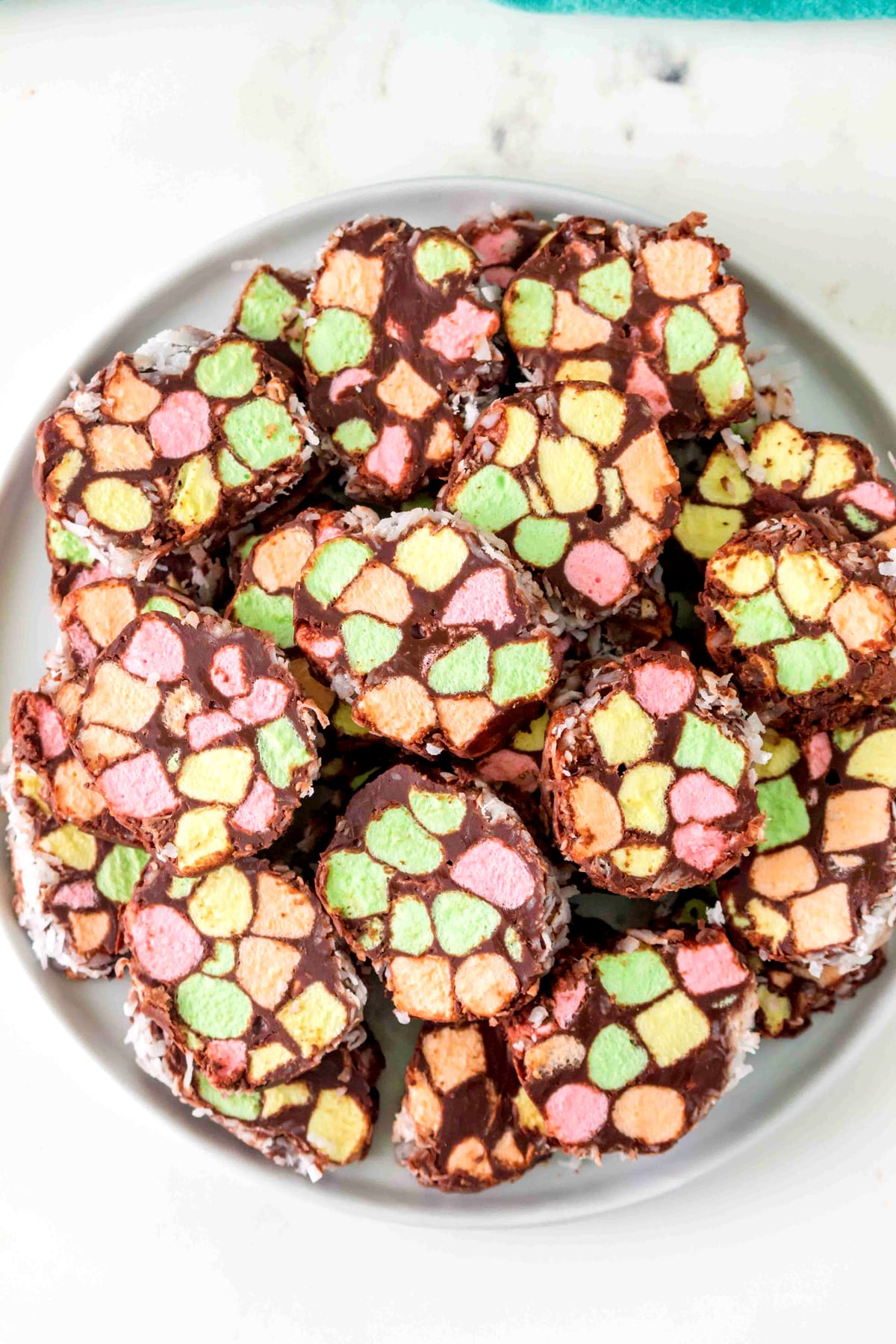 A plate of colorful Church Window Cookies coated in chocolate, arranged in a pile on a white dish.