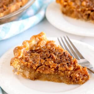 A slice of brown Ritz Cracker Pie with a crispy top is served on a white plate with a fork beside it.