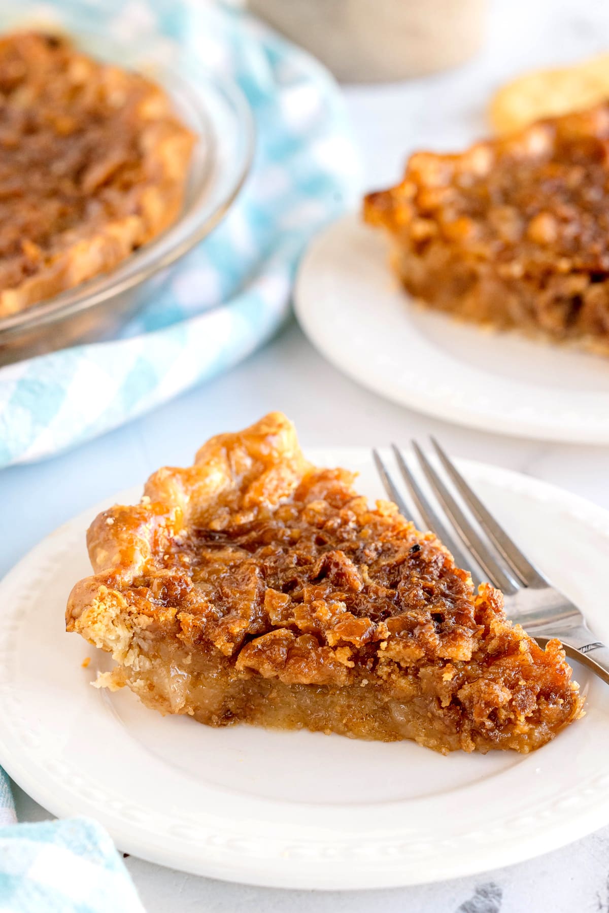 A slice of Ritz Cracker Pie on a white plate with a fork, with another slice and the remaining pie in the background.