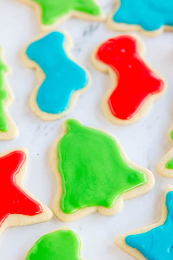 Assorted Christmas sugar cookies in shapes like stockings, bells, and stars, decorated with red, green, and blue icing, on a white surface.