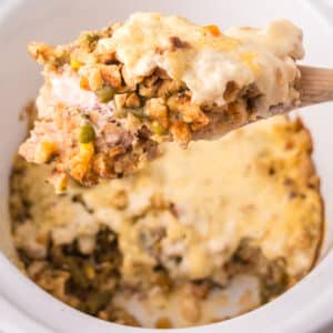 A wooden spoon lifts a serving of Chicken and Stuffing Casserole from a white dish, showing a crumbly, golden topping.
