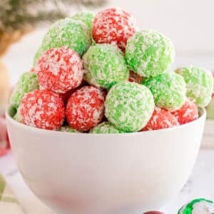 A white bowl filled with red and green Christmas Jello Balls is shown on a light surface.
