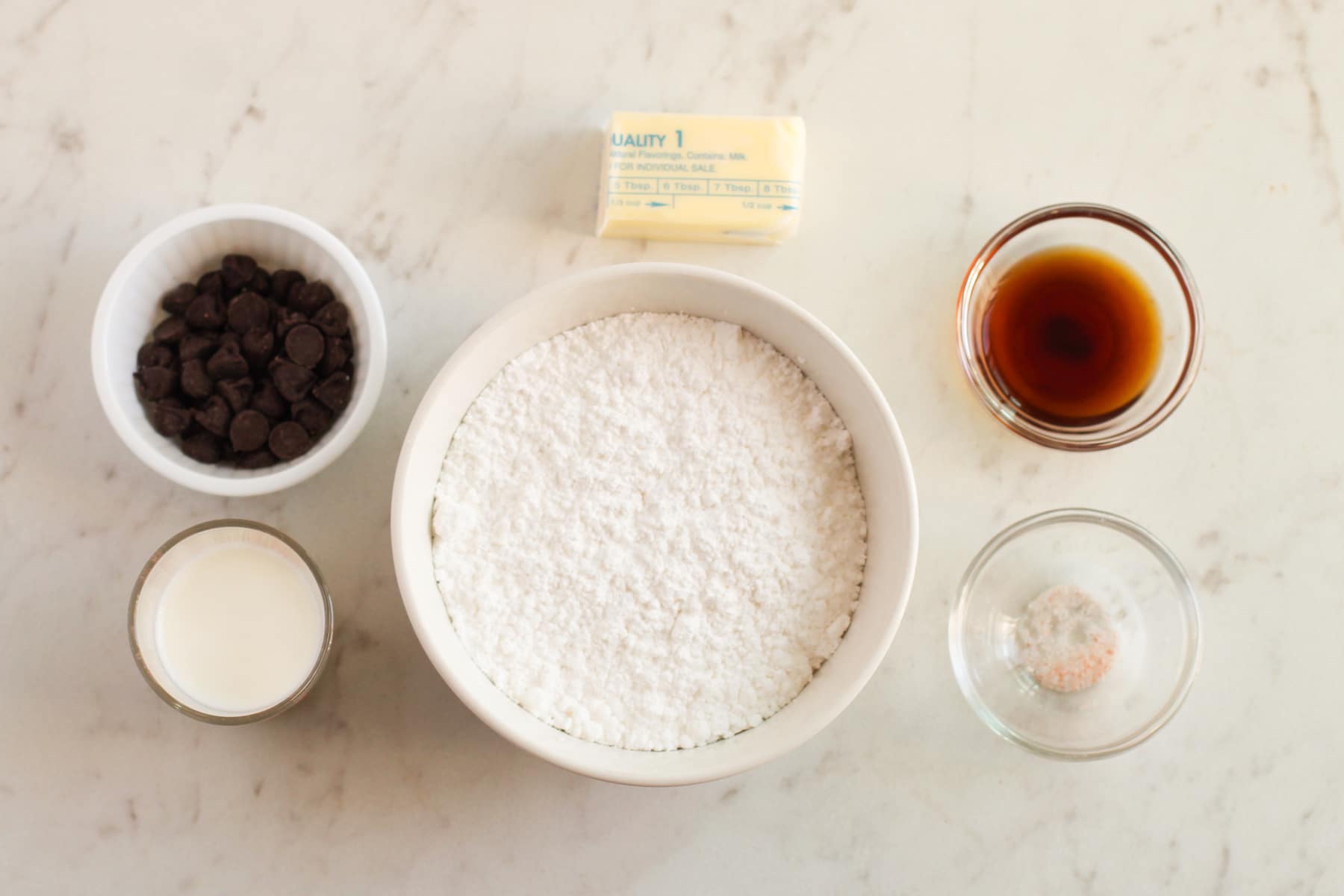 Baking ingredients for frosting of Fudgy Brownies on a marble surface, include: dark chocolate chips, butter, coffee, milk, sugar, and sea salt