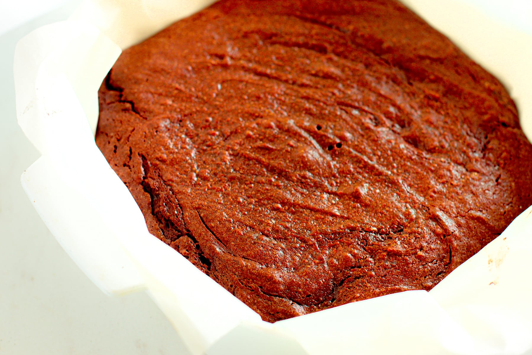 A close-up of a freshly baked Fudgy Brownies in a parchment-lined round pan.