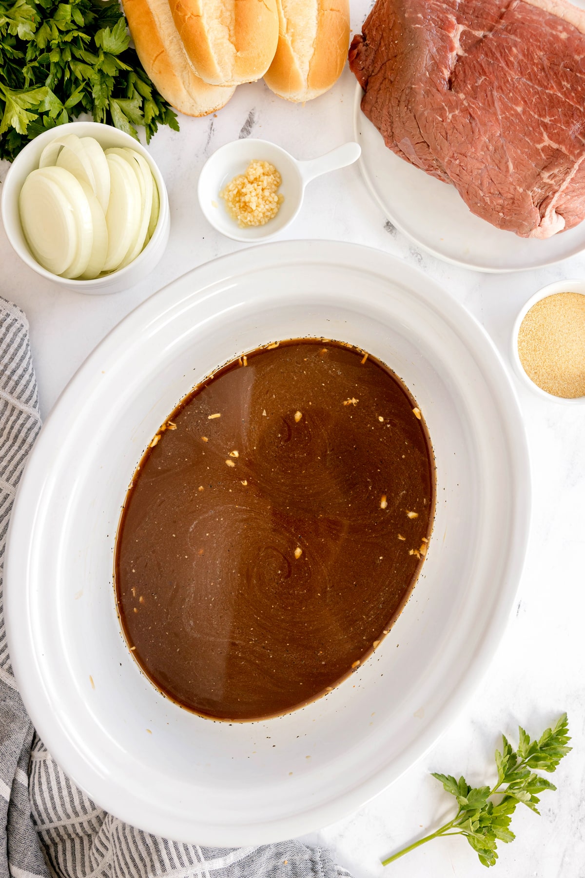 First step in preparing Slow Cooker French Dip Sandwiches is to pour the beef stock, Worcestershire sauce, salt, pepper, and onion soup mix into the bottom of the slow cooker.