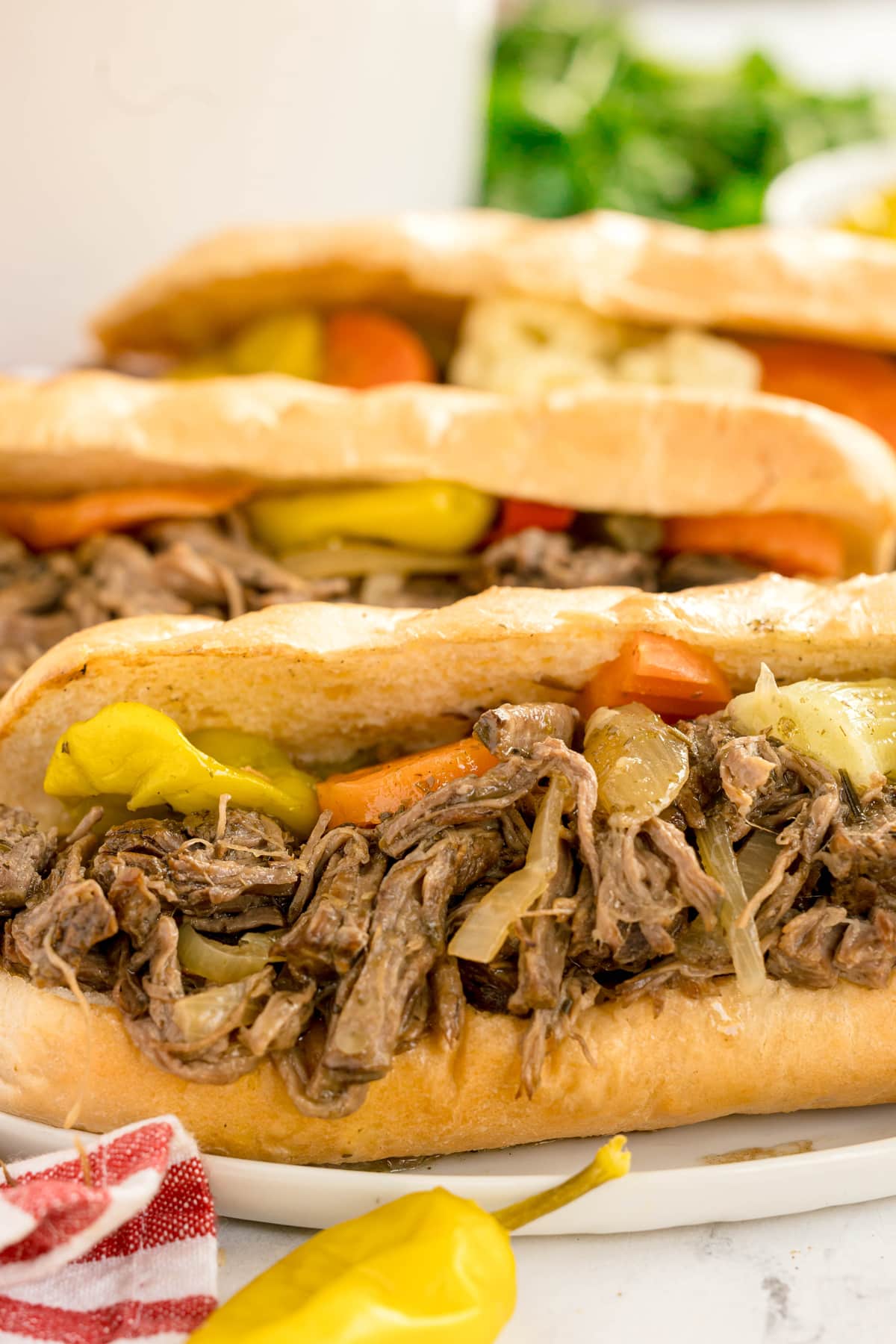 Close-up of Slow Cooker Italian Beef sandwiches filled with shredded beef, sliced carrots, peppers, and pickles on hoagie rolls.