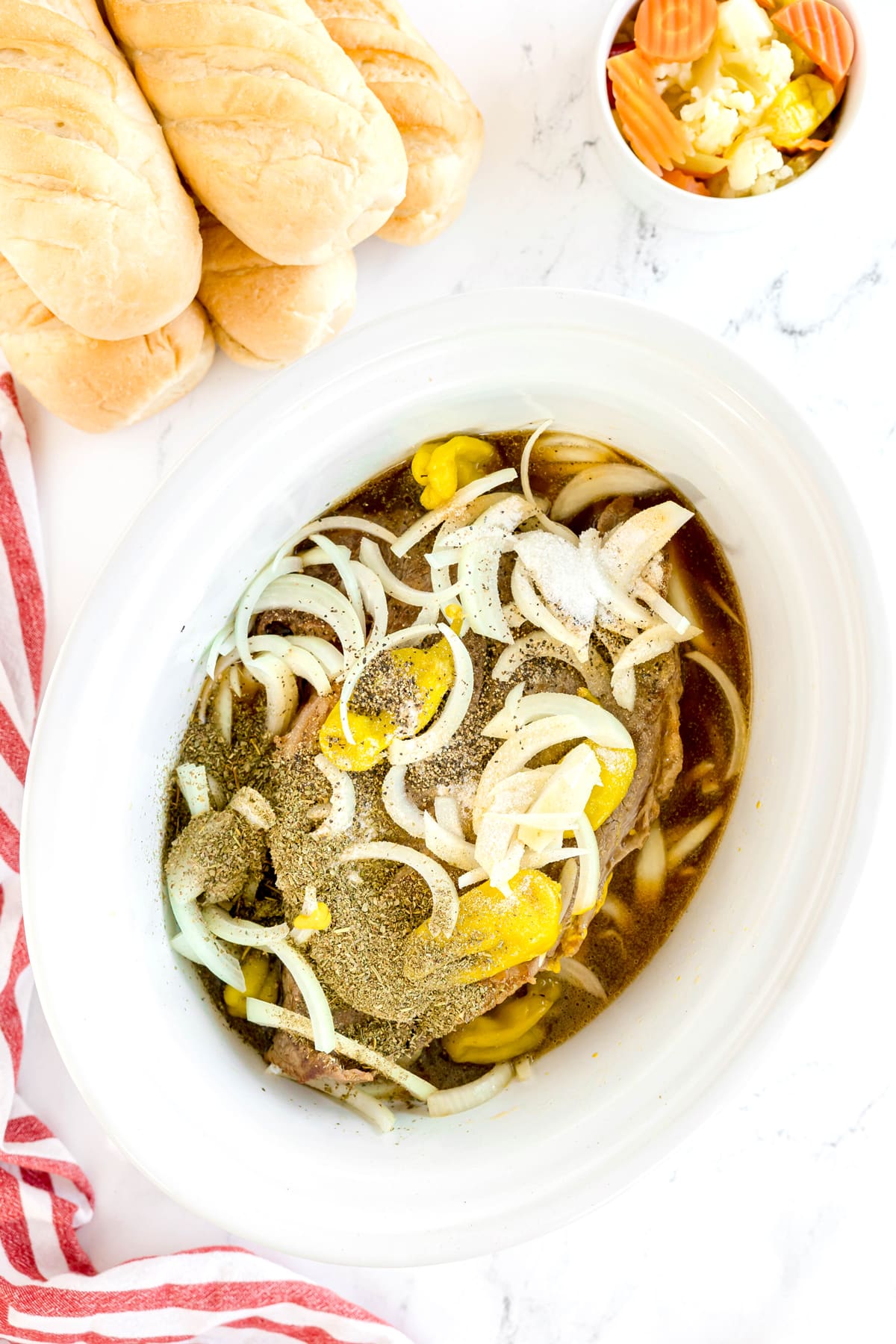 Next, for the Slow Cooker Italian Beef recipe, add the beef broth, pepperoncini juice, whole pepperoncini peppers, sliced onion, Italian seasoning, garlic powder, onion powder, sugar, salt, black pepper, and yellow mustard to the slow cooker, then gently stir to combine.