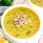 A bowl of Split Pea and Ham Soup topped with diced ham and chopped parsley, with a piece of bread and a napkin nearby.