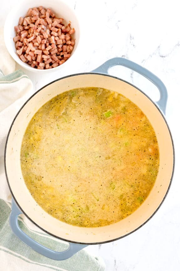 A large pot of Split Pea and Ham Soup with vegetables sits on the stove next to a bowl of diced ham.