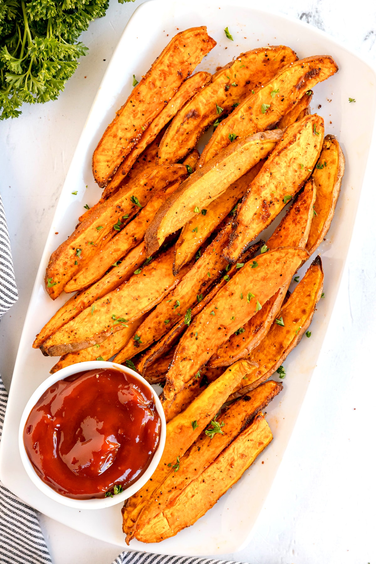Plate of Crispy Air Fryer Sweet Potato Wedges garnished with herbs, served with a small dish of ketchup on the side.