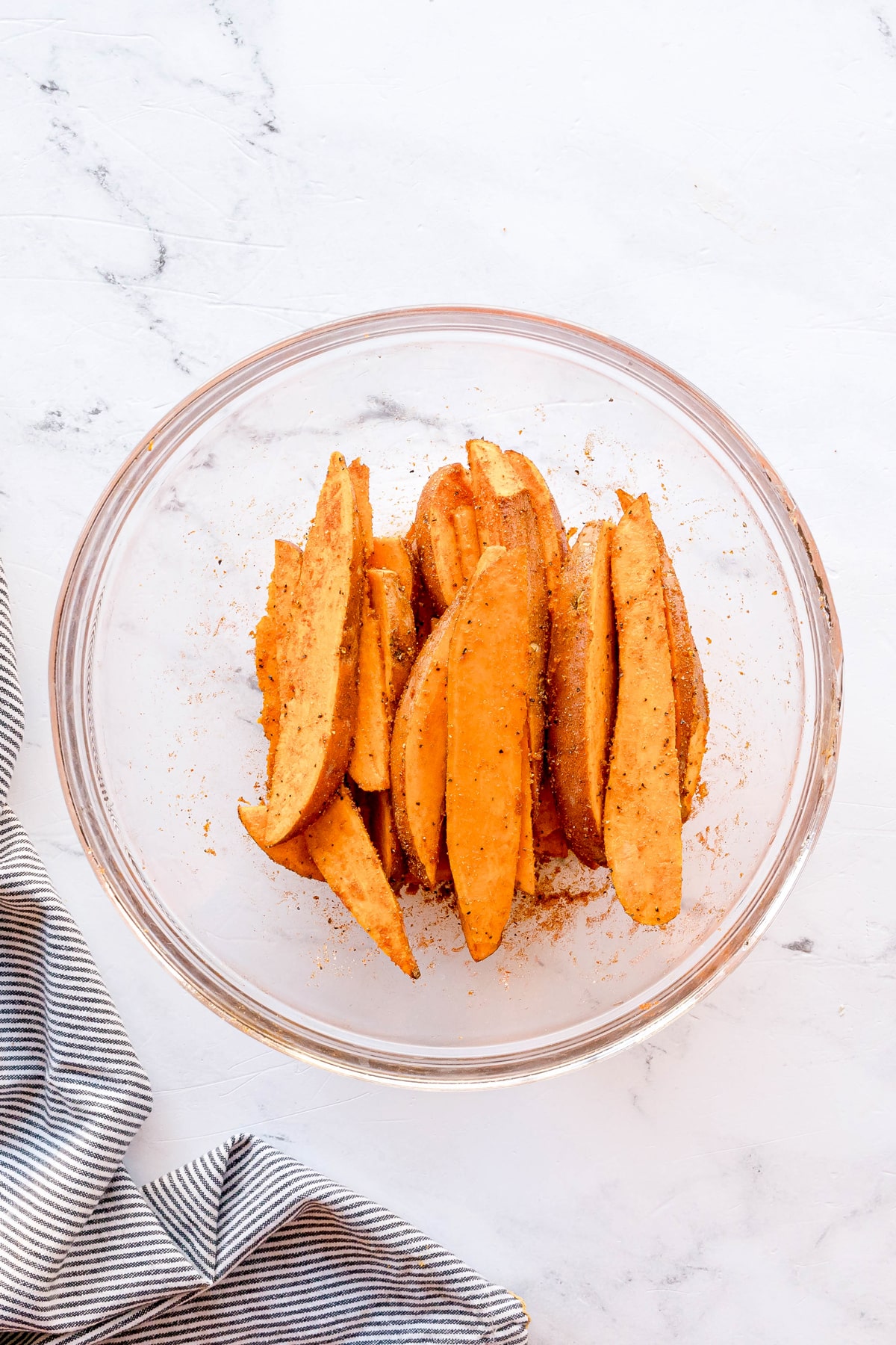Next step in preparing Crispy Air Fryer Sweet Potato Wedges is to add smoked paprika, garlic powder, onion powder, salt, and black pepper on a white marble surface next to a striped cloth.