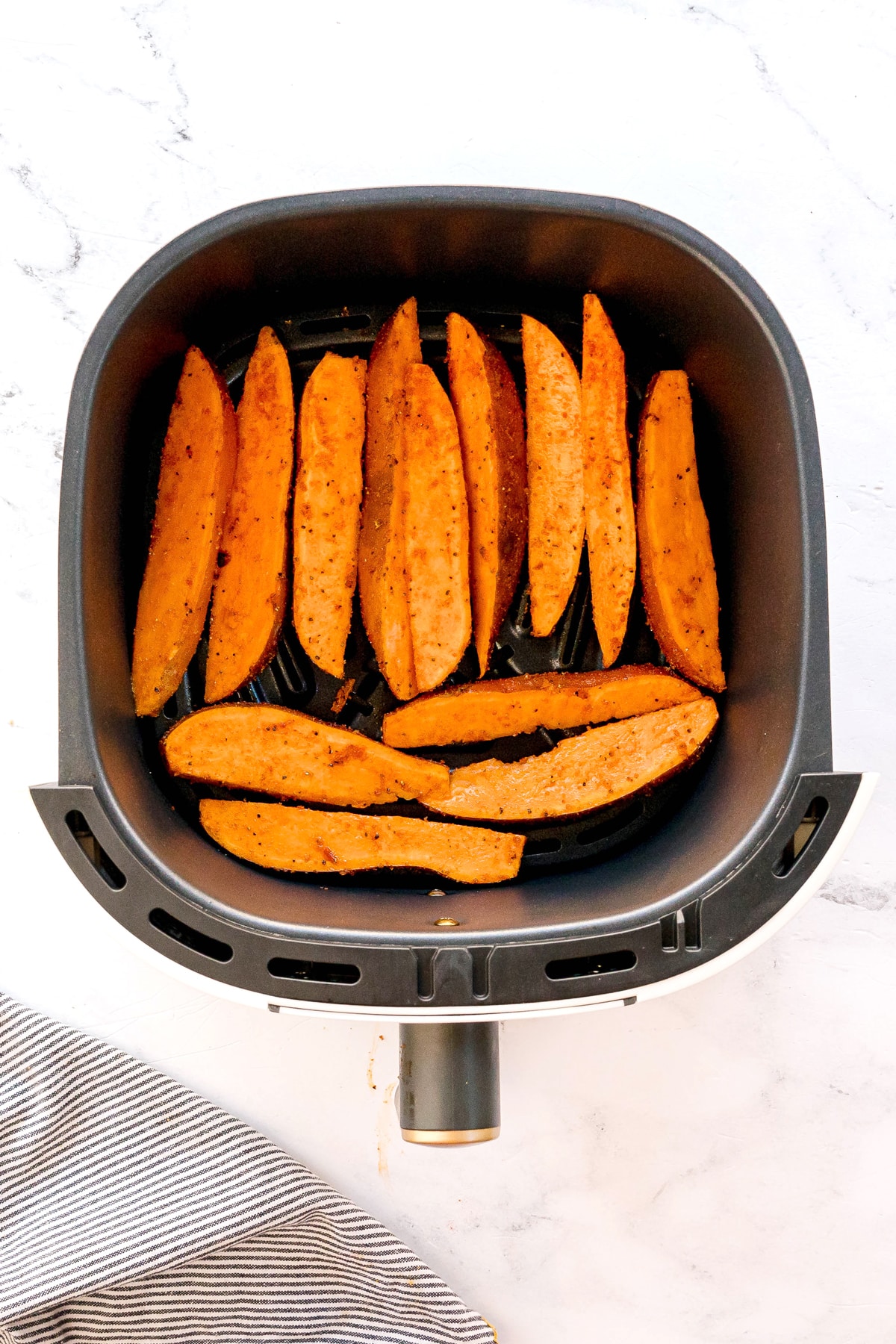 Sliced sweet potato wedges arranged in a single layer inside an air fryer basket, ready to be cooked. This is the next step in preparing Crispy Air Fryer Sweet Potato Wedges