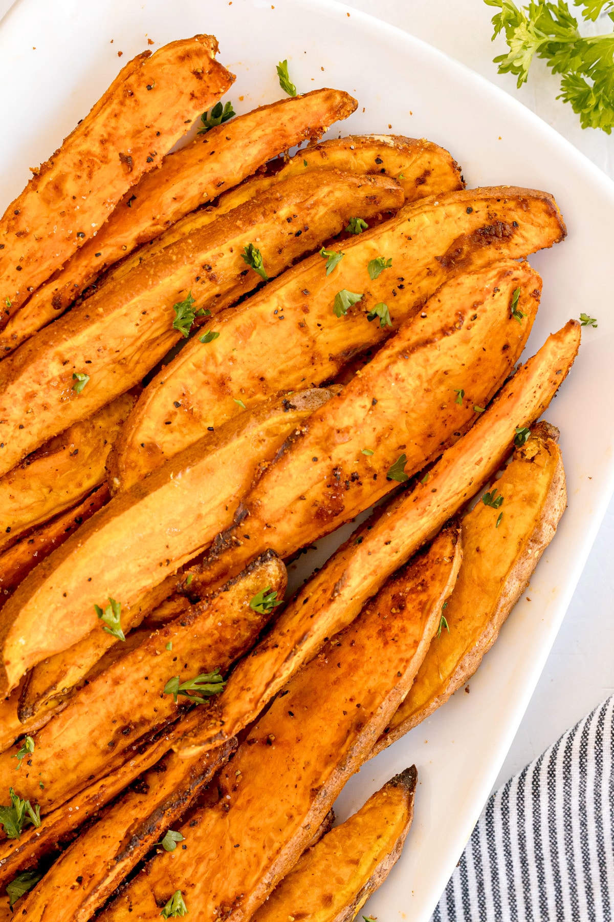 Air fryer Sweet Potato Wedges, sliced and roasted to perfection, are garnished with chopped parsley and served on a white plate.