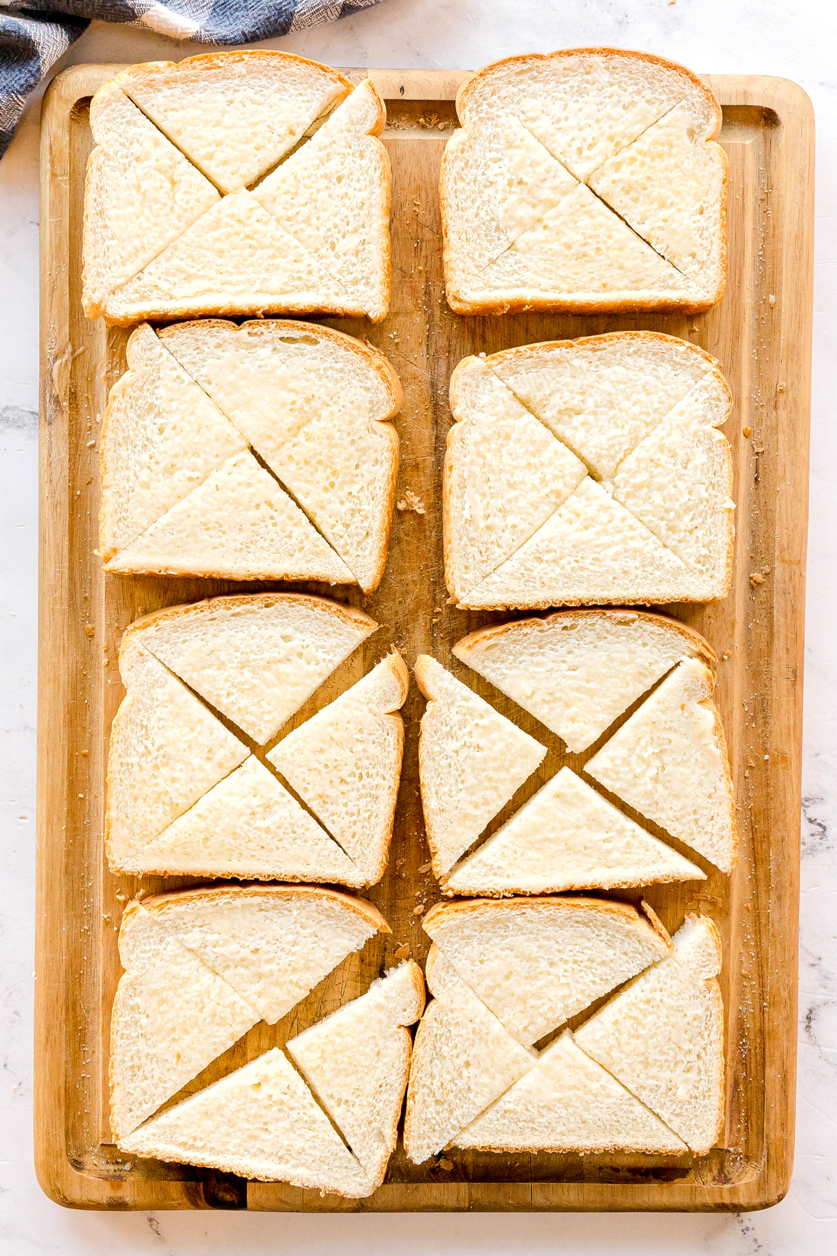 Eight slices of white bread on a wooden cutting board, each slice cut into four triangular pieces. This is for Nashville Hot Chicken Dip recipe.