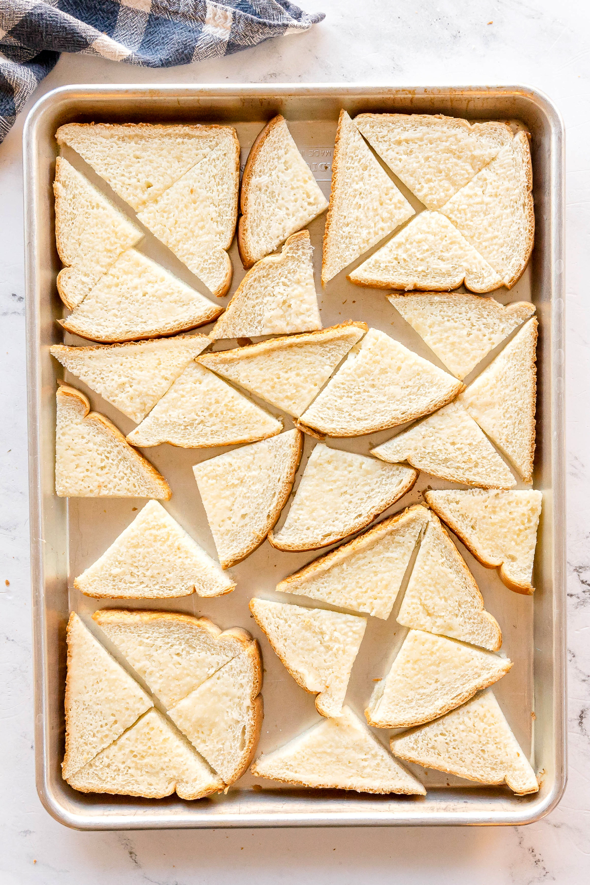 A baking sheet with slices of white bread for Nashville Hot Chicken Dip cut into triangles and arranged in a single layer on a marble surface.