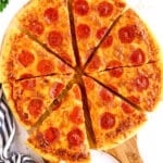 A whole Homemade Pepperoni Pizza cut into eight slices is displayed on a wooden pizza board.