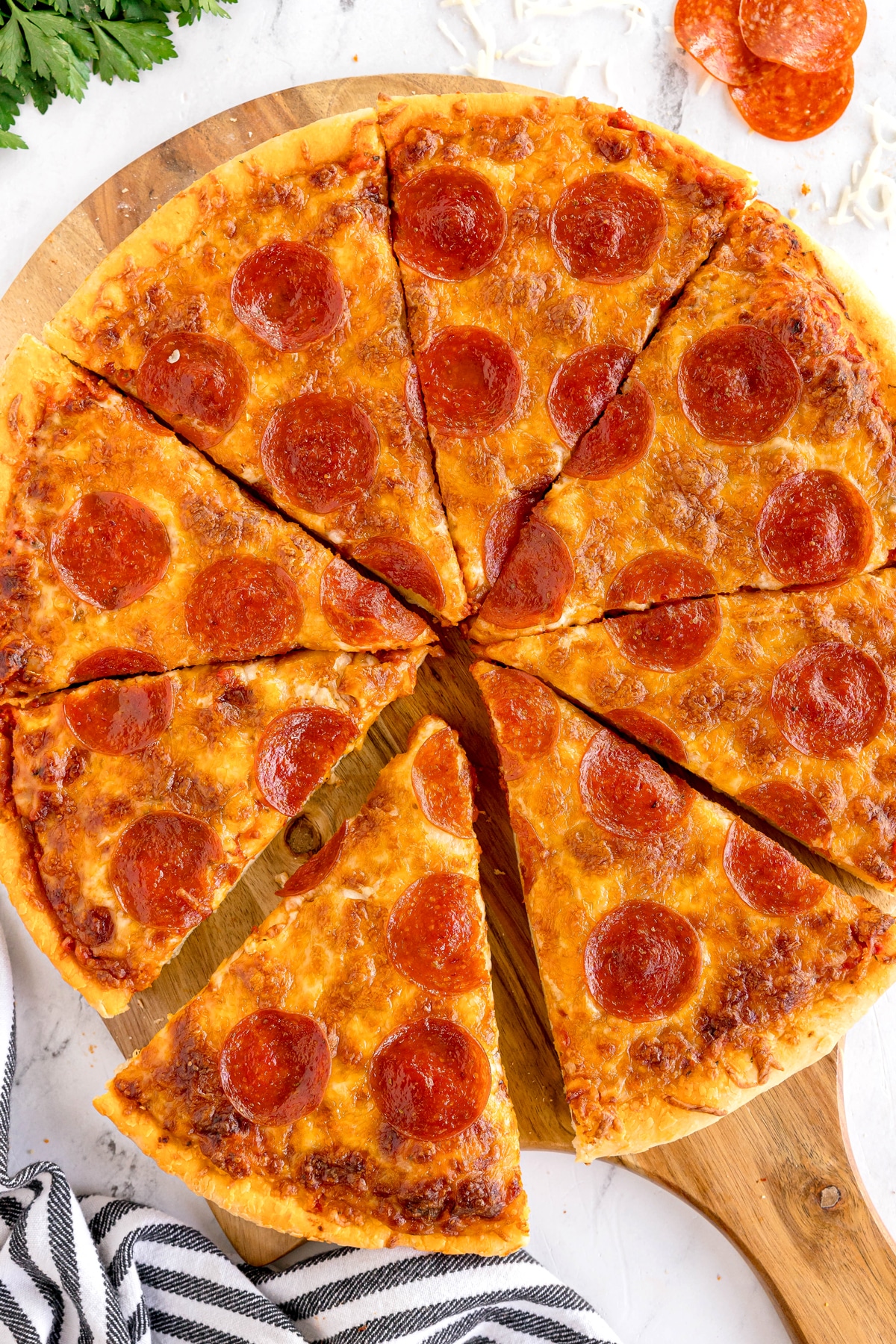 A Homemade Pepperoni Pizza cut into eight slices is displayed on a wooden board, with two slices pulled slightly away from the rest.