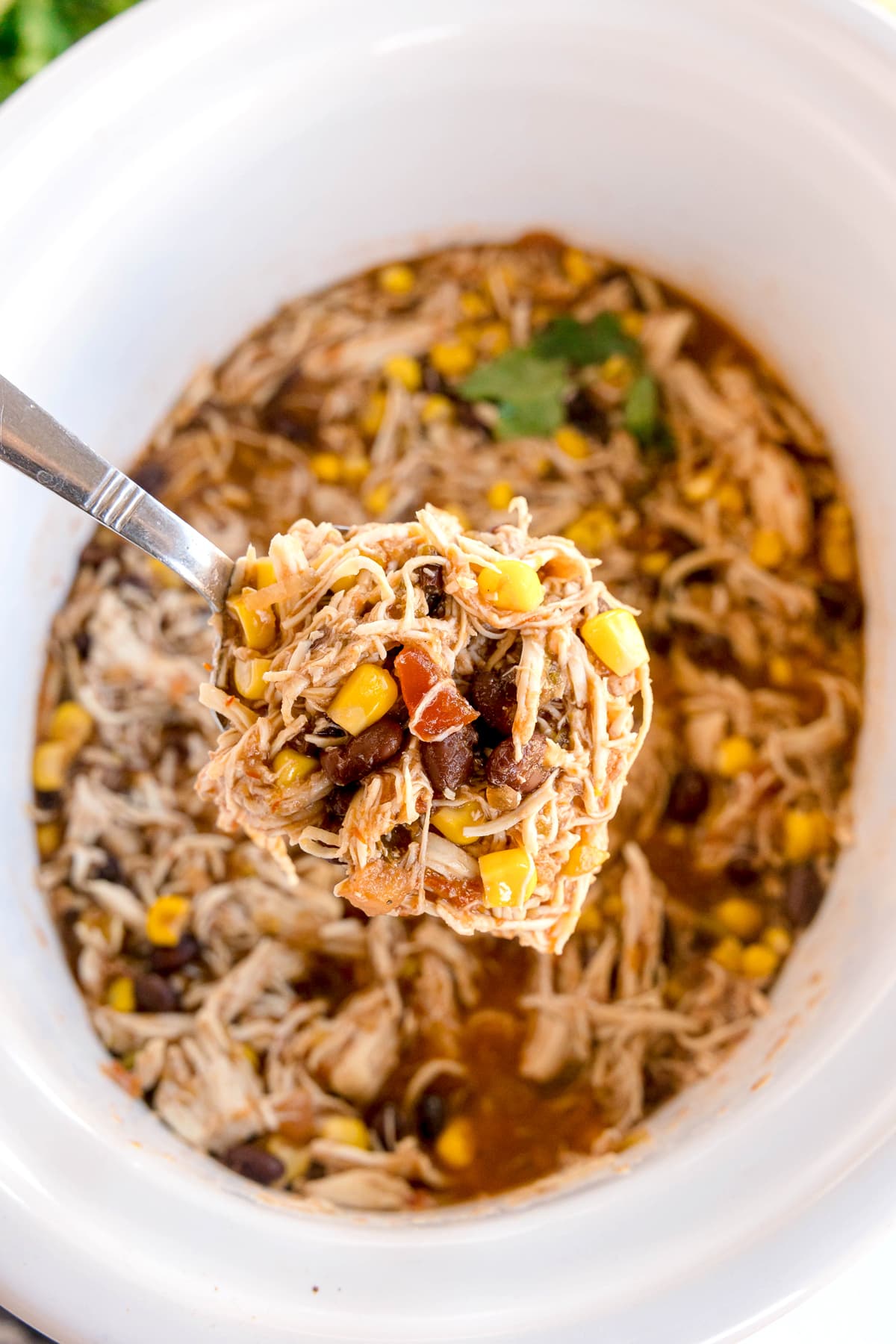 A spoonful of Slow Cooker Southwest Chicken shredded chicken, corn, black beans, and sauce held above a slow cooker filled with the same mixture.