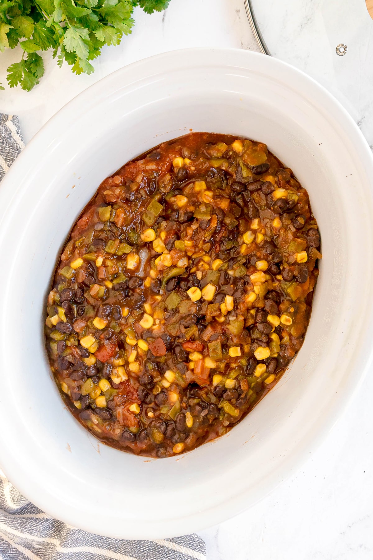 Adding a mixture of black beans, corn, tomatoes, and vegetables in a thick sauce in a slow cooker with chicken is one of the steps in preparing Slow Cooker Southwest Chicken