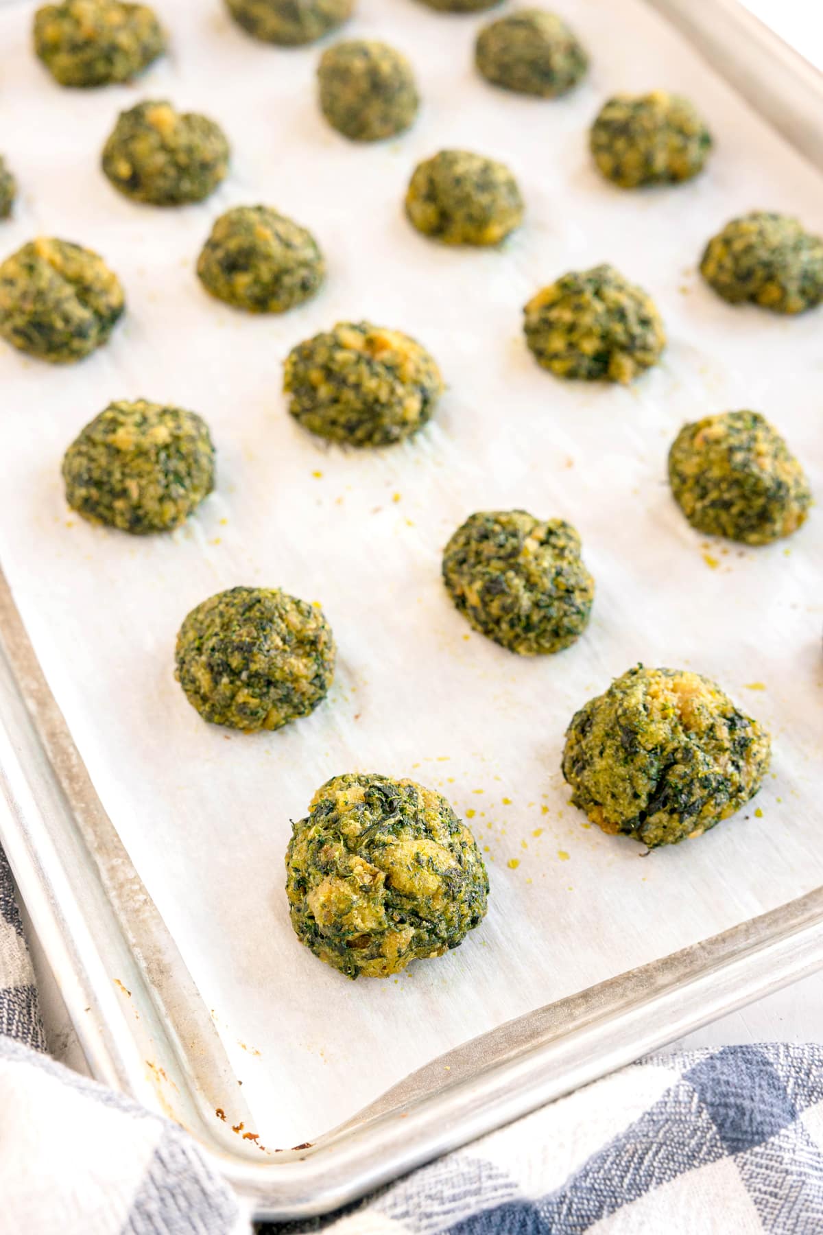 A baking sheet lined with parchment paper holds evenly spaced, round spinach balls, ready to be baked.