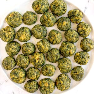 A white plate filled with evenly arranged green and yellow baked spinach balls on a white surface.