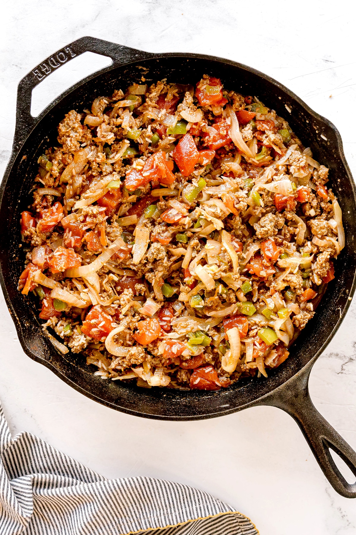 Next step is to add dice tomatoes in a cast iron skillet filled with cooked ground beef, onions, and bell peppers.