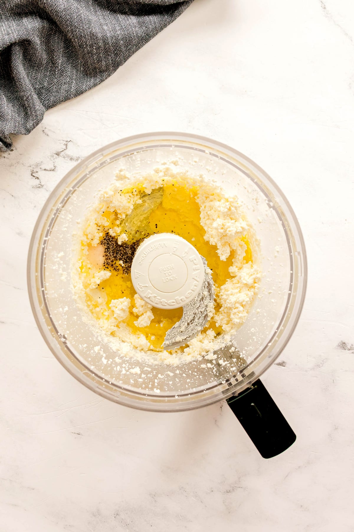 Next step in preparing Whipped Feta Tomato Crostini is to add olive oil, salt, and pepper to feta and cream cheese mixture.