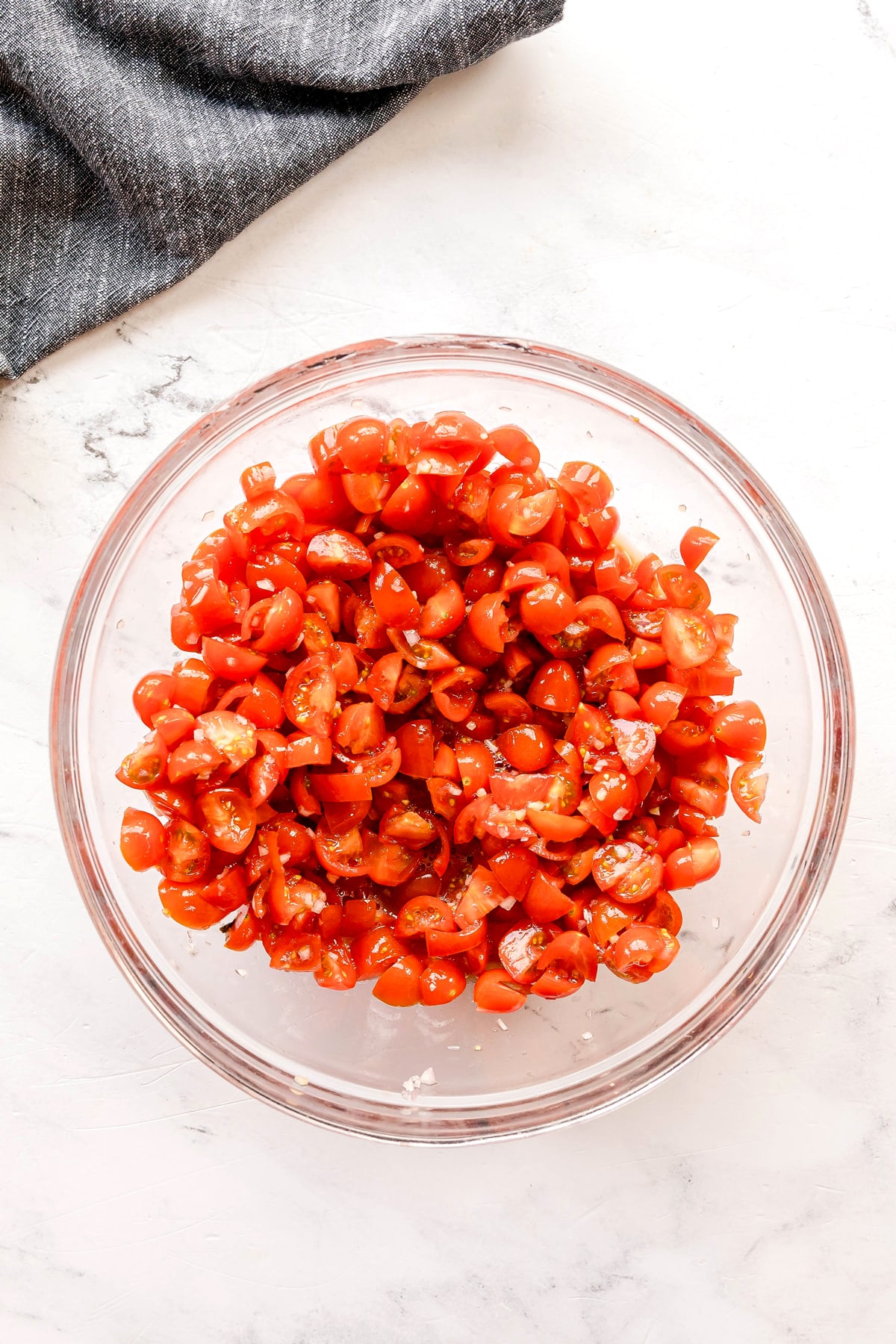 Next step in preparing Whipped Feta Tomato Crostini is to prepare tomatoes. Use a glass bowl filled with halved cherry tomatoes, seasoned with shallots, garlic, red wine vinegar and then add olive oil, salt and pepper.