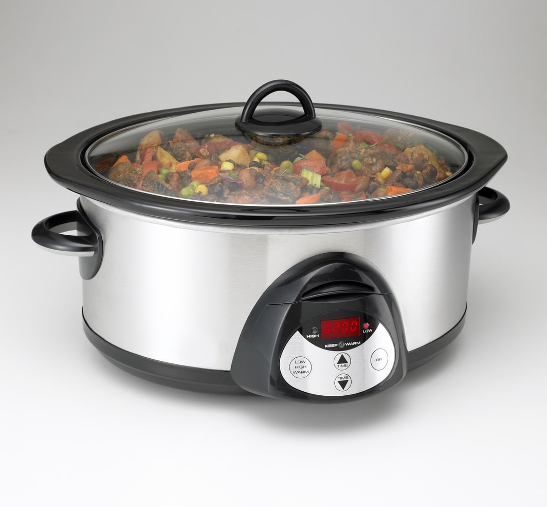 A stainless steel slow cooker filled with a stew of meat and vegetables, with a digital display and control buttons on the front.