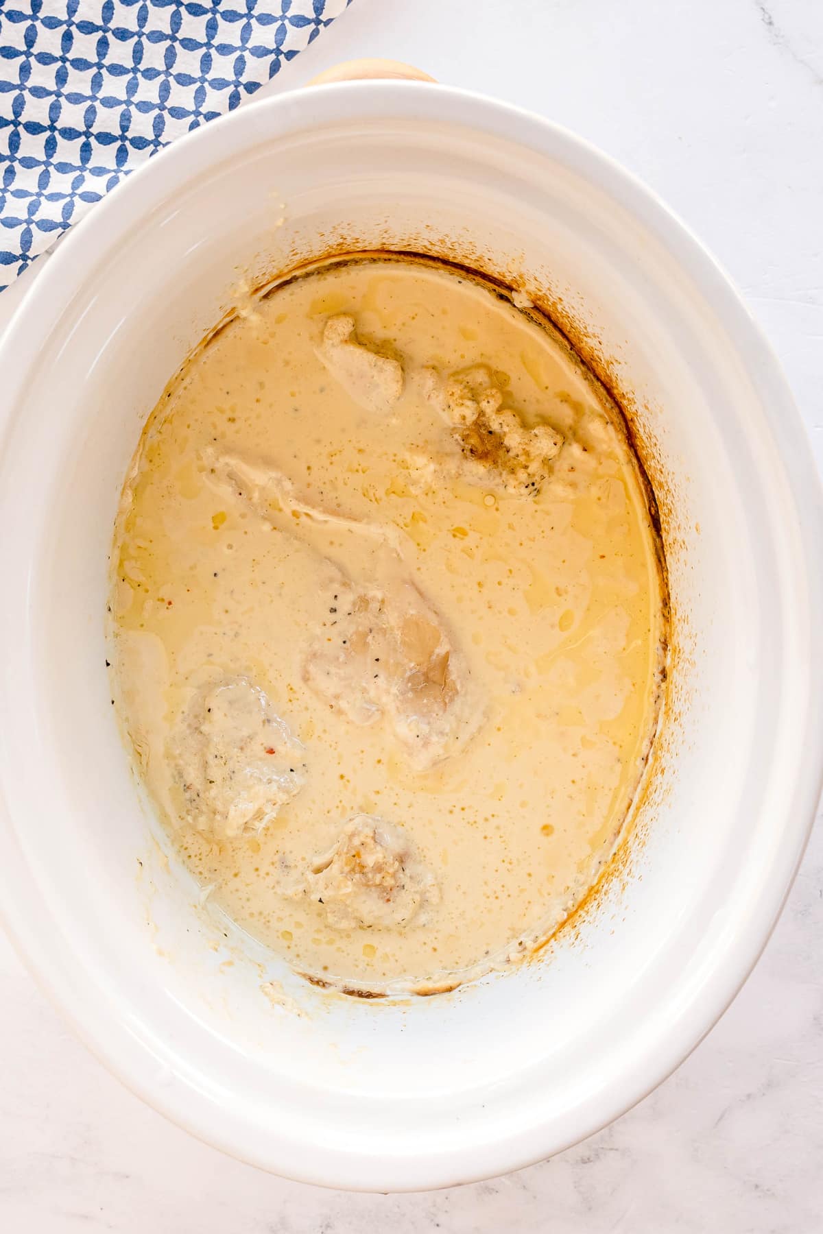 Slow Cooker Creamy Italian Chicken with some browning along the edges. Blue and white patterned cloth partially visible in the corner.